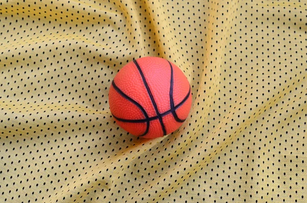 Small Orange Rubber Basketball Lies Yellow Sport Jersey Clothing Fabric — Stock Photo, Image