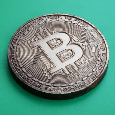 Fiziksel bitcoin şeklinde çikolata ürün yeşil bir plastik arka plan üzerinde yatıyor. Yenilebilir formdaki Kripto biriminin modeli