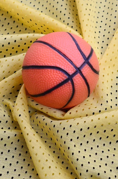 Piccola pallacanestro in gomma arancione si trova su una maglia sportiva gialla clo — Foto Stock