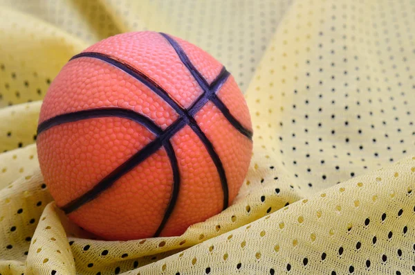 Pequeno basquete de borracha laranja encontra-se em um clo camisola esporte amarelo — Fotografia de Stock