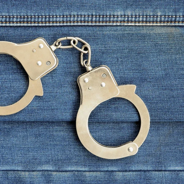 警察鋼のダークブルーのジーンズ背景に横たわっている手錠 — ストック写真