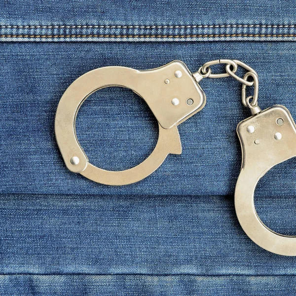 警察鋼のダークブルーのジーンズ背景に横たわっている手錠 — ストック写真