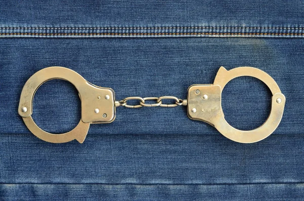 Полицейские стальные наручники лежат на фоне темно-синих джинсов — стоковое фото