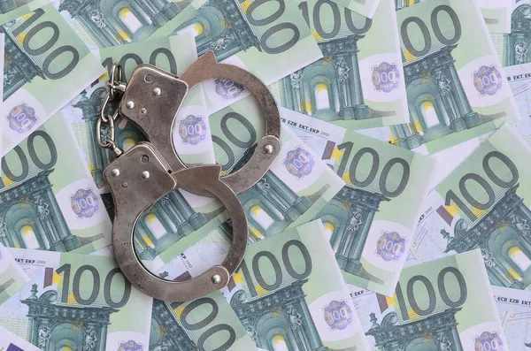 Die Handschellen der Polizei klickten auf einem grünen Geldschein im Wert von 100 Euro. Viel Geld bildet einen unendlichen Haufen — Stockbild Polizeihandschellen liegen auf einer Reihe grüner Geldscheine. — Stockfoto