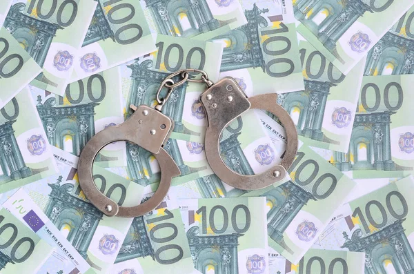 Die Handschellen der Polizei klickten auf einem grünen Geldschein im Wert von 100 Euro. Viel Geld bildet einen unendlichen Haufen — Stockbild Die Handschellen Der Polizei Klickten Auf Einem Grünen Geldschein Wert — Stockfoto