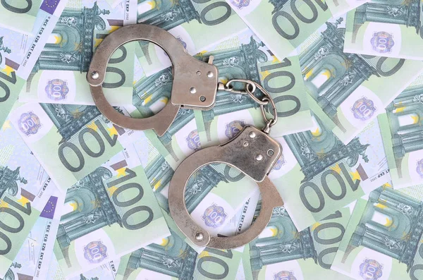 Die Handschellen der Polizei klickten auf einem grünen Geldschein im Wert von 100 Euro. Viel Geld bildet einen unendlichen Haufen — Stockbild Polizeihandschellen liegen auf einer Reihe grüner Geldscheine. — Stockfoto