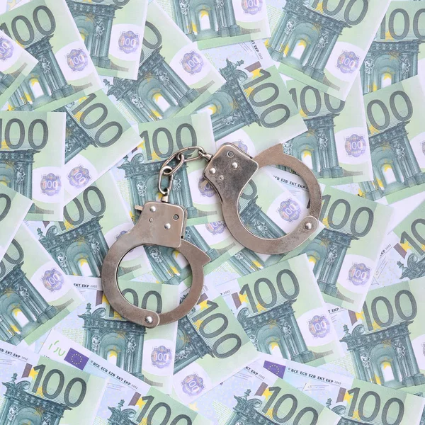 Die Handschellen der Polizei klickten auf einem grünen Geldschein im Wert von 100 Euro. Viel Geld bildet einen unendlichen Haufen — Stockbild Die Handschellen Der Polizei Klickten Auf Einem Grünen Geldschein Wert — Stockfoto