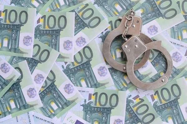 Die Handschellen der Polizei klickten auf einem grünen Geldschein im Wert von 100 Euro. Viel Geld bildet einen unendlichen Haufen — Stockbild Die Handschellen Der Polizei Klickten Auf Einem Grünen Geldschein Wert — Stockfoto