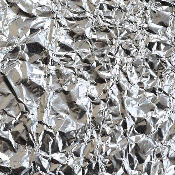 Thin wrinkled sheet of crushed tin aluminum silver foil background with shiny crumpled surface for texture