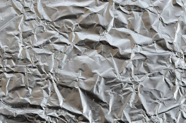 Thin wrinkled sheet of crushed tin aluminum silver foil background with shiny crumpled surface for texture