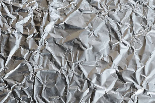 Thin wrinkled sheet of crushed tin aluminum silver foil background with shiny crumpled surface for texture