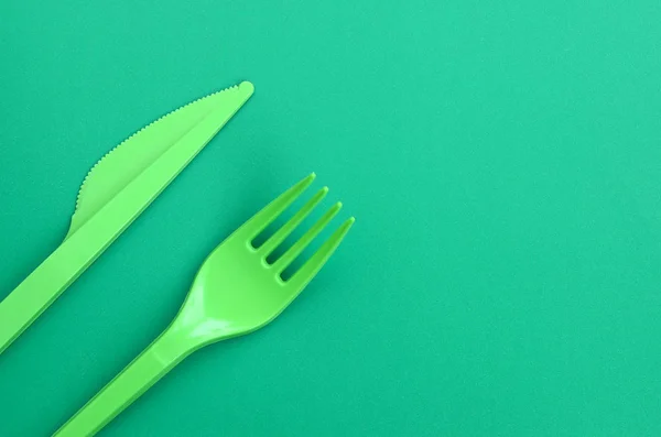 使い捨てのプラスチック製食器グリーン 緑の背景の表面に横にプラスチックのフォークとナイフ — ストック写真