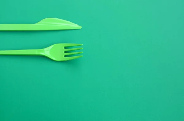 Disposable plastic cutlery green. Plastic fork and knife lie on a green background surface