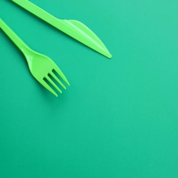 使い捨てのプラスチック製食器グリーン 緑の背景の表面に横にプラスチックのフォークとナイフ — ストック写真