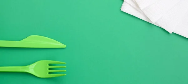 Disposable plastic cutlery green. Plastic fork and knife lie on a green background surface next to napkins