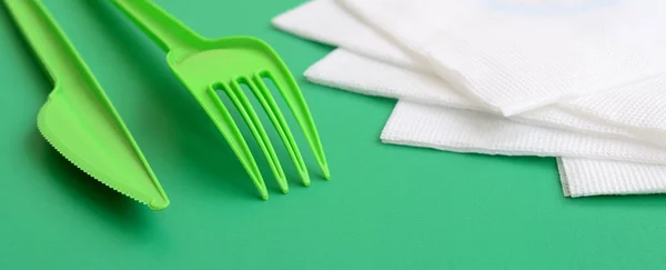 Disposable plastic cutlery green. Plastic fork and knife lie on a green background surface next to napkins