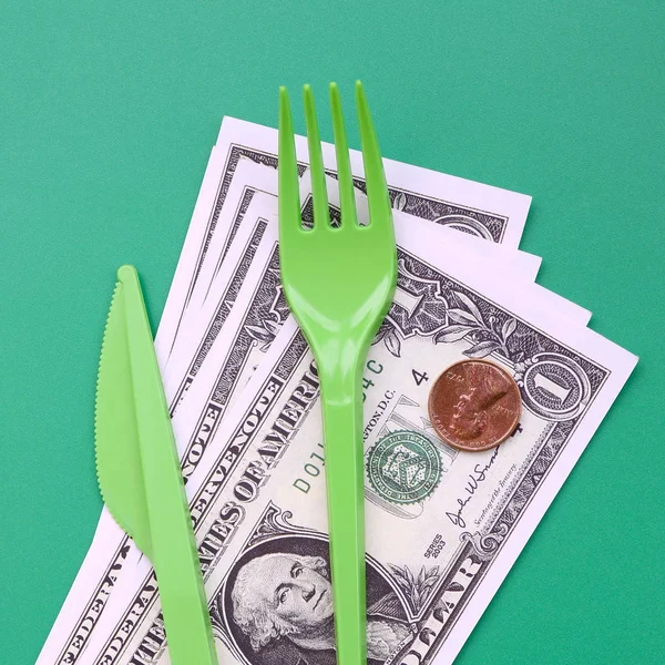 Disposable plastic cutlery green. Plastic fork and knife lie on a small amount of US dollars