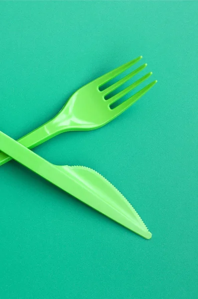 Disposable plastic cutlery green. Plastic fork and knife lie on a green background surface