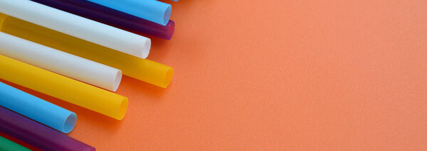 Many colorful straws for drinks lies on a bright orange background surface