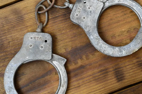 Старые ржавые полицейские наручники лежат на поцарапанной деревянной поверхности — стоковое фото
