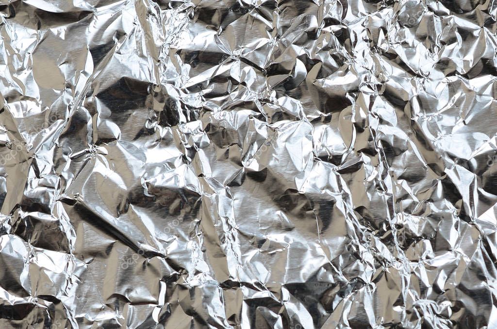 Thin wrinkled sheet of crushed tin aluminum silver foil background with shiny crumpled surface for texture