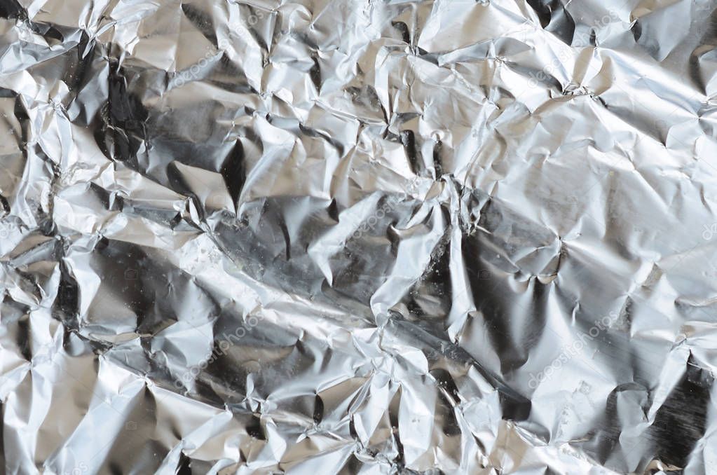 Thin wrinkled sheet of crushed tin aluminum silver foil background with shiny crumpled surface for texture