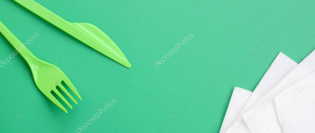 Disposable plastic cutlery green. Plastic fork and knife lie on a green background surface next to napkins