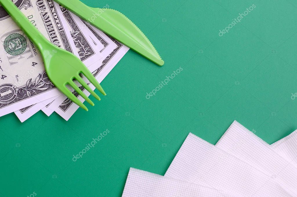 Disposable plastic cutlery green. Plastic fork and knife lie on a small amount of US dollars next to napkins