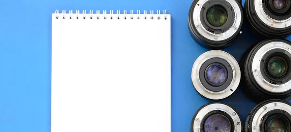Több Fotográfiai Lencsék Fehér Notebook Feküdjön Egy Fényes Kék Háttér — Stock Fotó