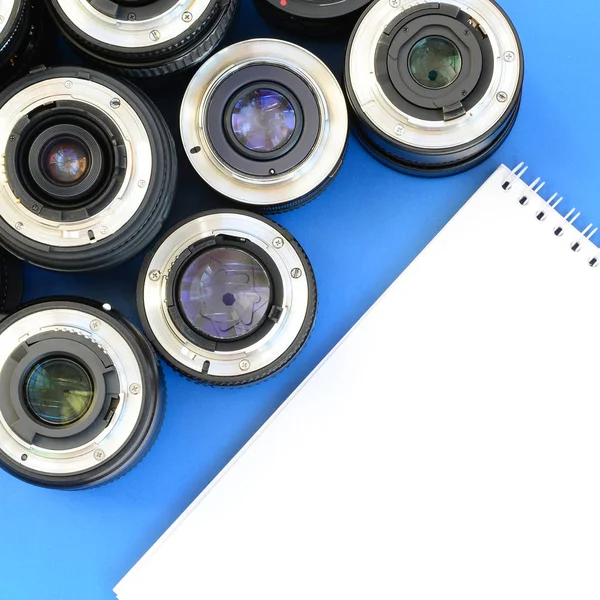 Several Photographic Lenses White Notebook Lie Bright Blue Background Space — Stock Photo, Image