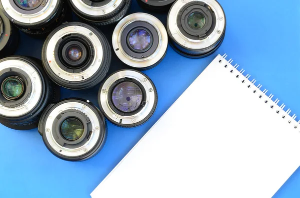 Több Fotográfiai Lencsék Fehér Notebook Feküdjön Egy Fényes Kék Háttér — Stock Fotó