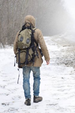 Bir insan büyük bir sırt çantası ile kışın kar fırtınası sırasında bir banliyö asfalt yolda yürüyor