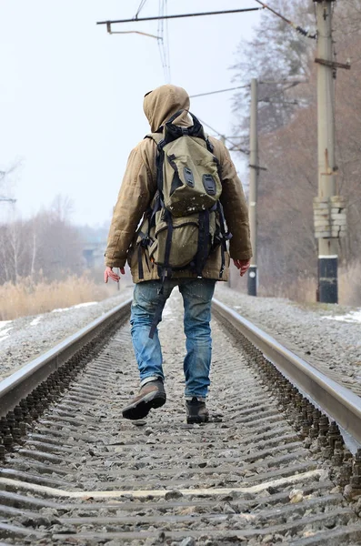 A man with a large backpack goes ahead on the railway track during the winter season