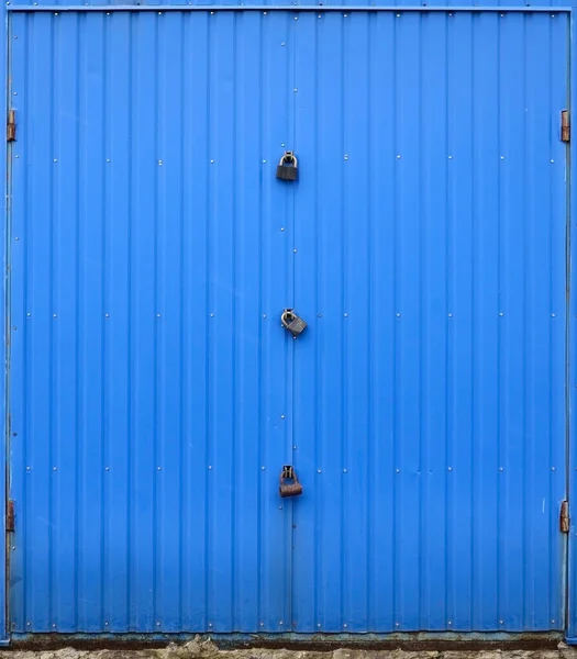 Texture of a metal blue wall with a gate closed for three locks