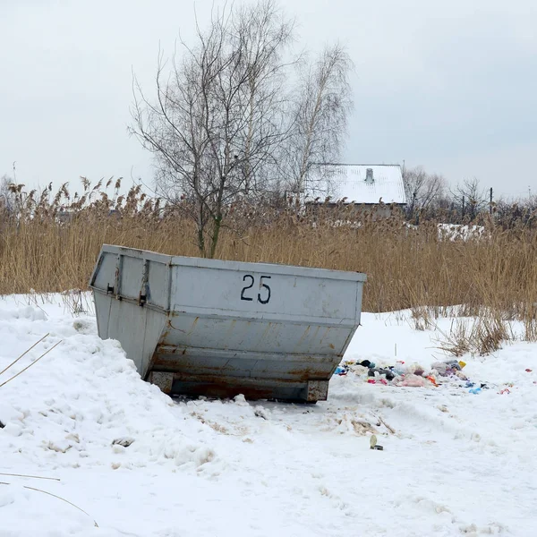 Trash bin at the side of street in winter with lip garbage container winter snow. Metal container for household waste