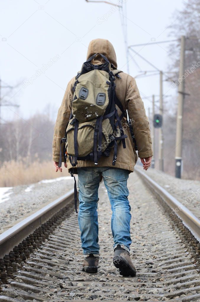 A man with a large backpack goes ahead on the railway track during the winter season