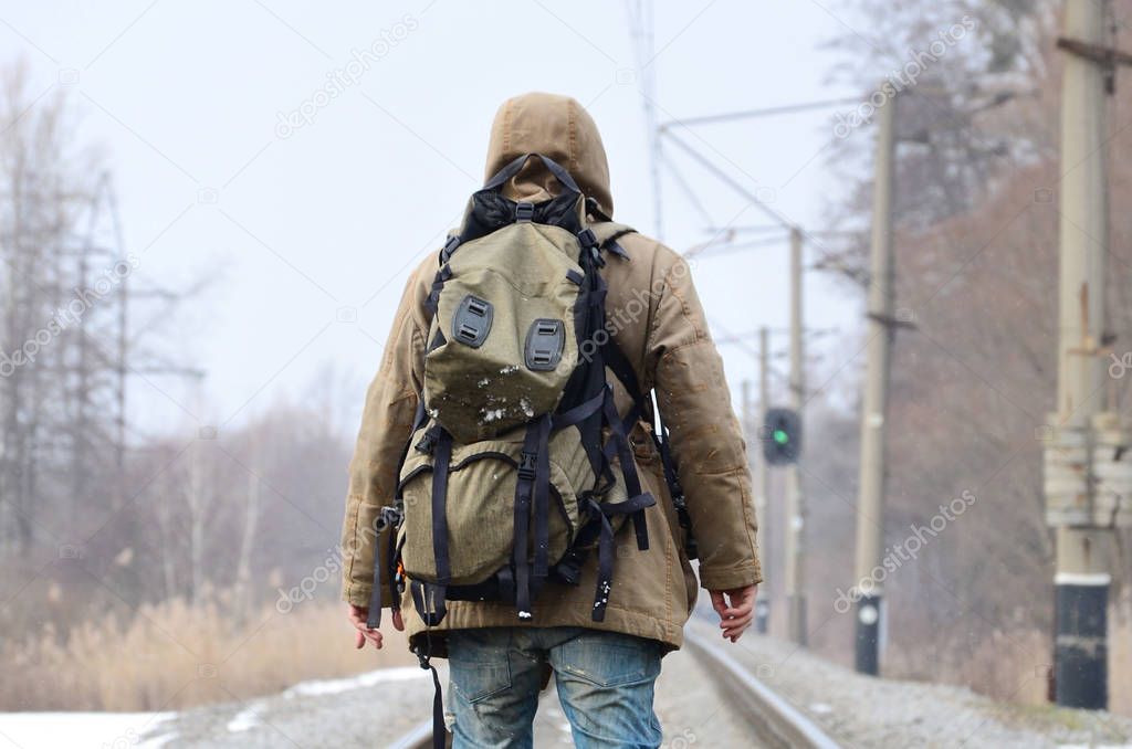A man with a large backpack goes ahead on the railway track during the winter season