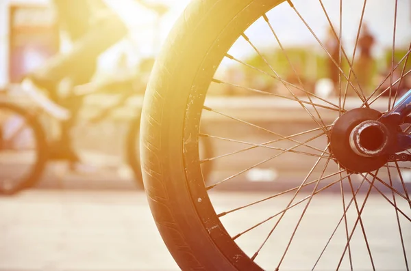 A BMX bike wheel against the backdrop of a blurred street with cycling riders. Extreme Sports Concept