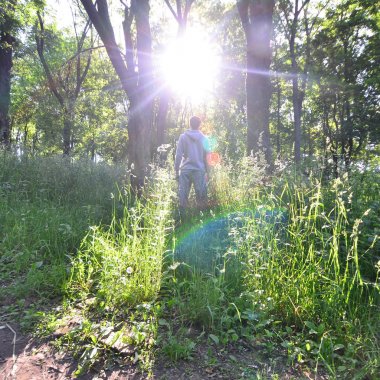 Bir gri spor takım elbise standları ormandaki ağaçlar arasında güneş karşısında genç bir adam. Rekreasyon spor sırasında açık hava ormanda çalıştırın. Rapture güzel şafak