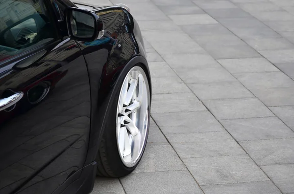 グレーのタイルの正方形上に立っている白いホイールと黒の光沢のある車の斜めビュー — ストック写真