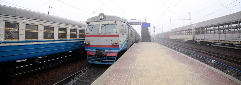 The railway track in a misty morning. The Ukrainian suburban train is at the passenger station. Fisheye photo with increased distortion