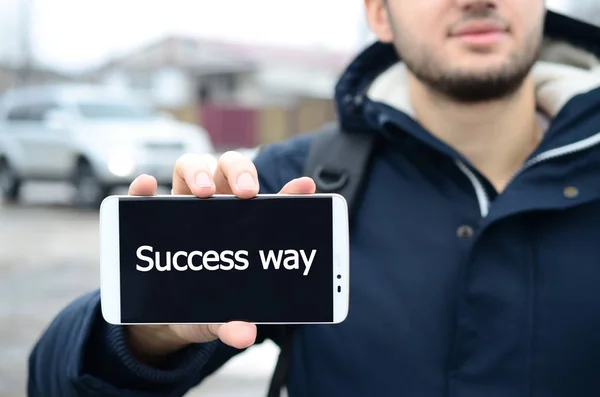 A young guy shows an inscription on the smartphone's display on — Stock Photo, Image