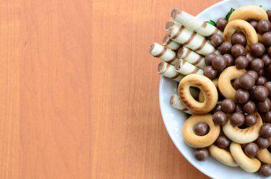 Gevrek tübüllerin, çikolata eritme topları ve simit ahşap bir masa üzerinde beyaz bir tabak içinde yalan. Çeşitli tatlılar karışımı
