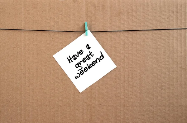 Have a great weekend. Note is written on a white sticker that hangs with a clothespin on a rope on a background of brown cardboard