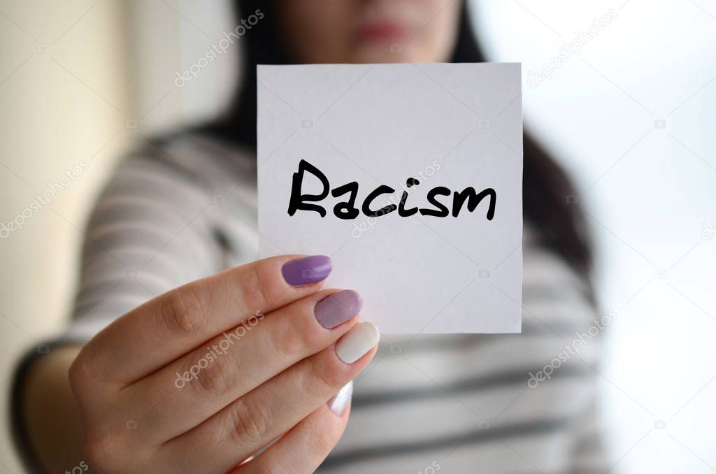 Young sad girl shows a white sticker. Caucasian brunette holding a sheet of paper with message. Racism
