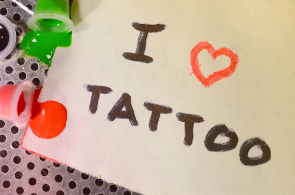 I love tattoo. The text is written on a small sheet of paper next to the overturned caps with colored tattoo ink