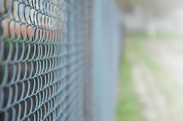 A photograph of a metal net used as a fence of private possessions. Old metal grid in perspective with a blurred background