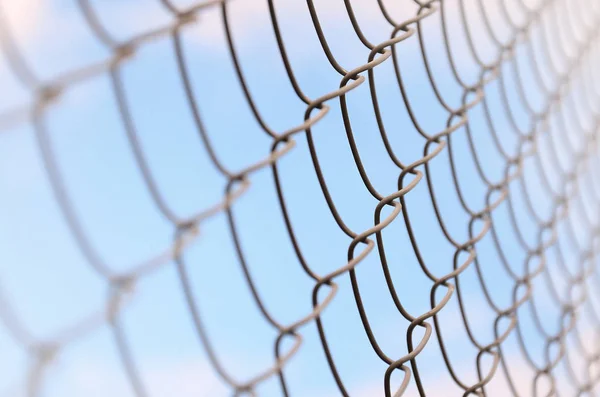 A photograph of a metal net used as a fence of private possessions. Old metal grid in perspective with a blurred background
