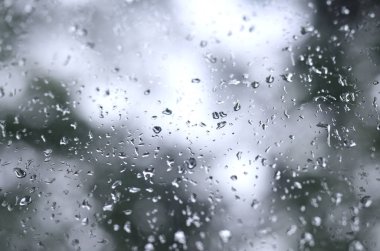 Çiçek açması yeşil ağaçların bulanık manzaralı pencere camına bir fotoğraf yağmur bırakır. Soyut resim bulutlu ve yağmurlu hava koşulları gösterilen