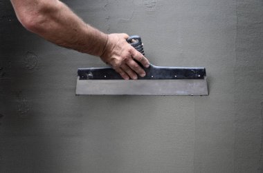 Ev yenilenen araçları sıvama duvar ile eski bir işçi elleri. Sıvacı yenilenen açık duvar ve spatula ve alçı ile köşeleri. Duvar izolasyonu. İnşaat bitirme işleri